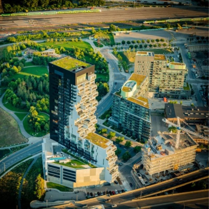 Aerial view of modern buildings with green roofs, surrounded by lush trees and roads. Construction site visible, conveying urban development and innovation.